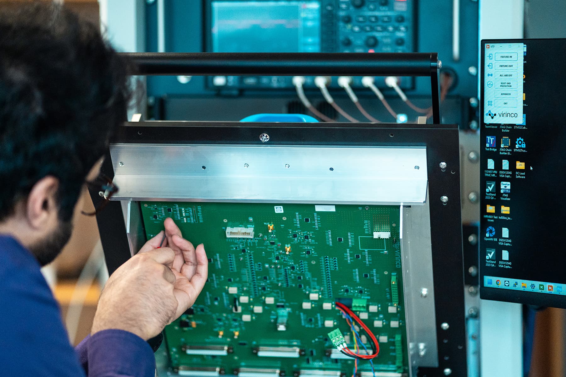 An engineer probing a PCB inside an open Virinco test fixture, with the fixture-control software visible.