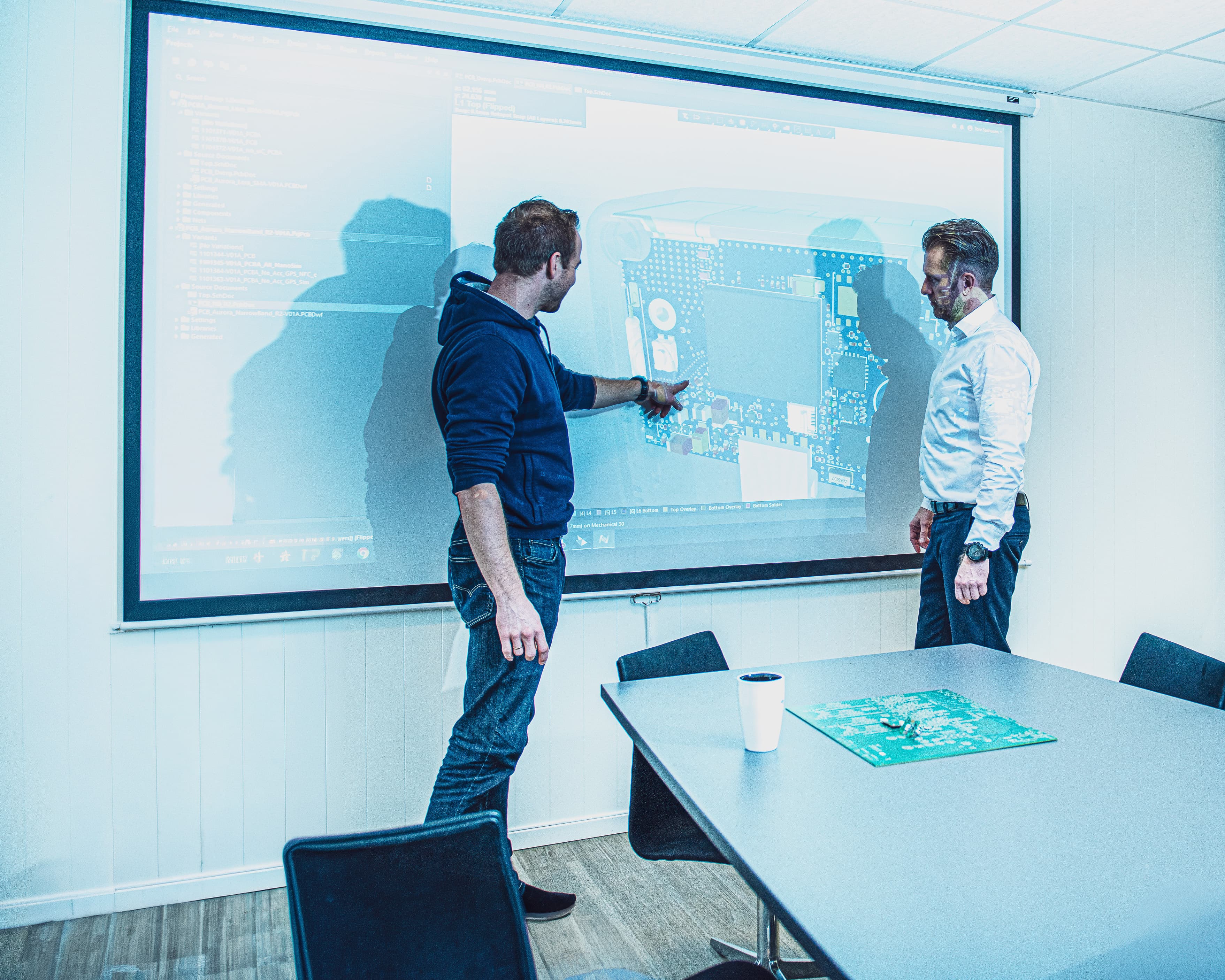 Two engineers reviewing a PCB design on screen in a design review meeting.